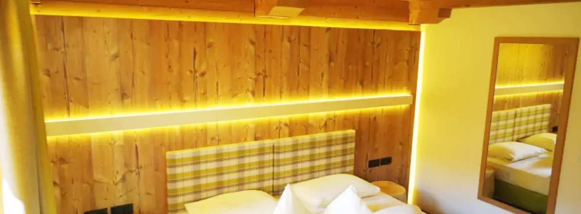 Hotelzimmer mit Holzdecken und -wänden, indirekter Beleuchtung und Nachttischen aus Baumstämmen