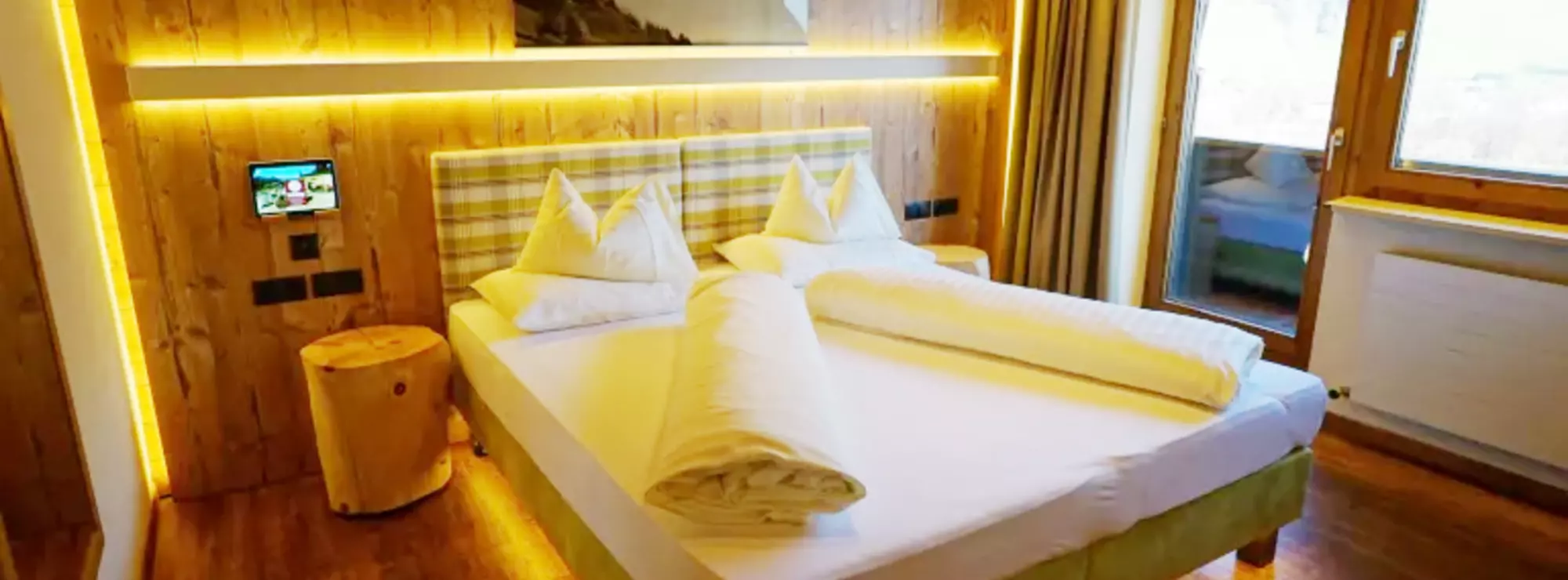 Hotelzimmer mit holzvertäfelter Wand, indirekter Nachtischbeleuchtung und Balkon
