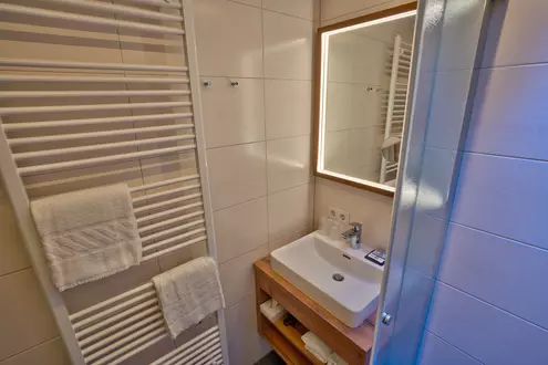Bad mit beleuchtetem Spiegel, kleinem Waschtisch und Handtuchtrockner