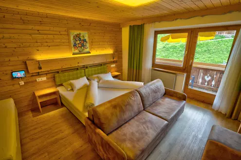 Hotelzimmer mit Wänden und Decke aus Holz, Zustellbett, Sofa und Balkon