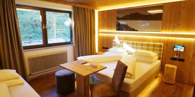 Schlafzimmer mit Wänden und Decke aus Holz, kleinem Schreibtisch und Zustellbett