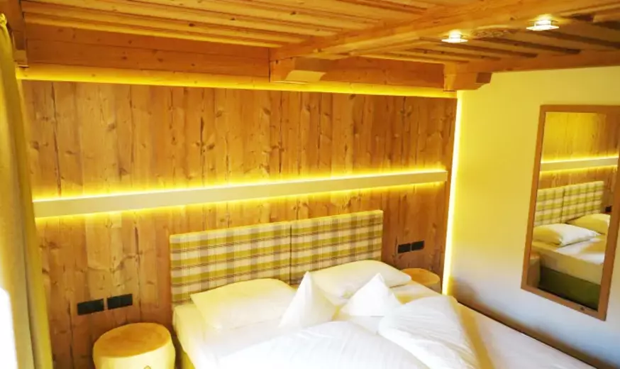 Hotelzimmer mit Holzdecken und -wänden, indirekter Beleuchtung und Nachttischen aus Baumstämmen